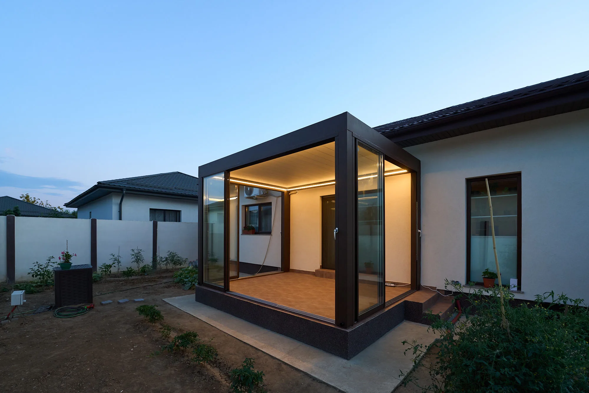 Bioclimatic pergola with glass enclosure and LED lighting, seen from the garden at dusk