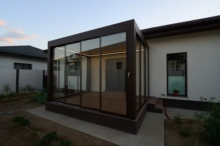Brown aluminium bioclimatic pergola with glass enclosure in daylight