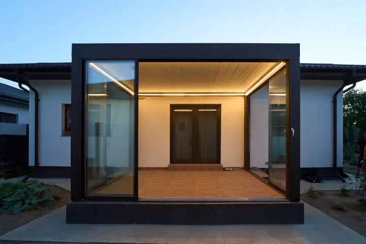 Façade of the glass-enclosed terrace with bioclimatic pergola, in the evening