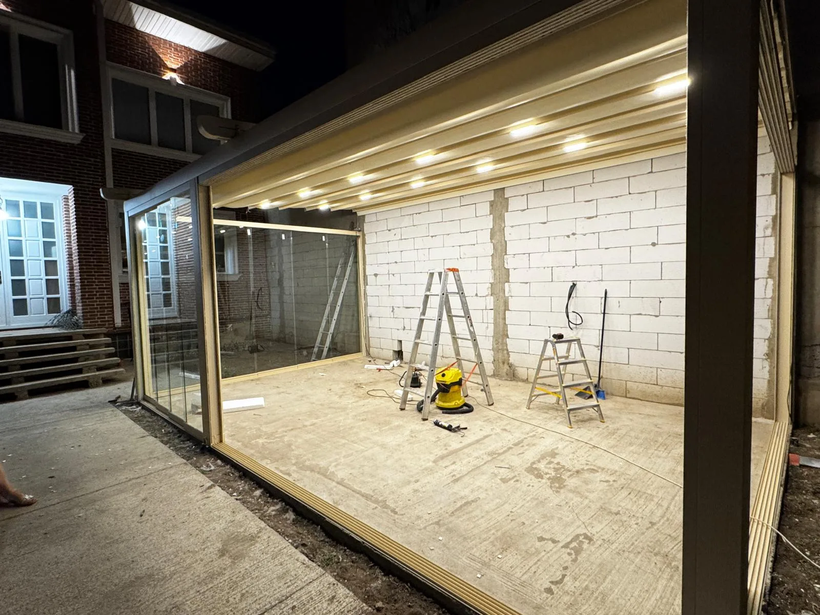 Wave retractable pergola with LED spotlights on and glass enclosure, in the evening
